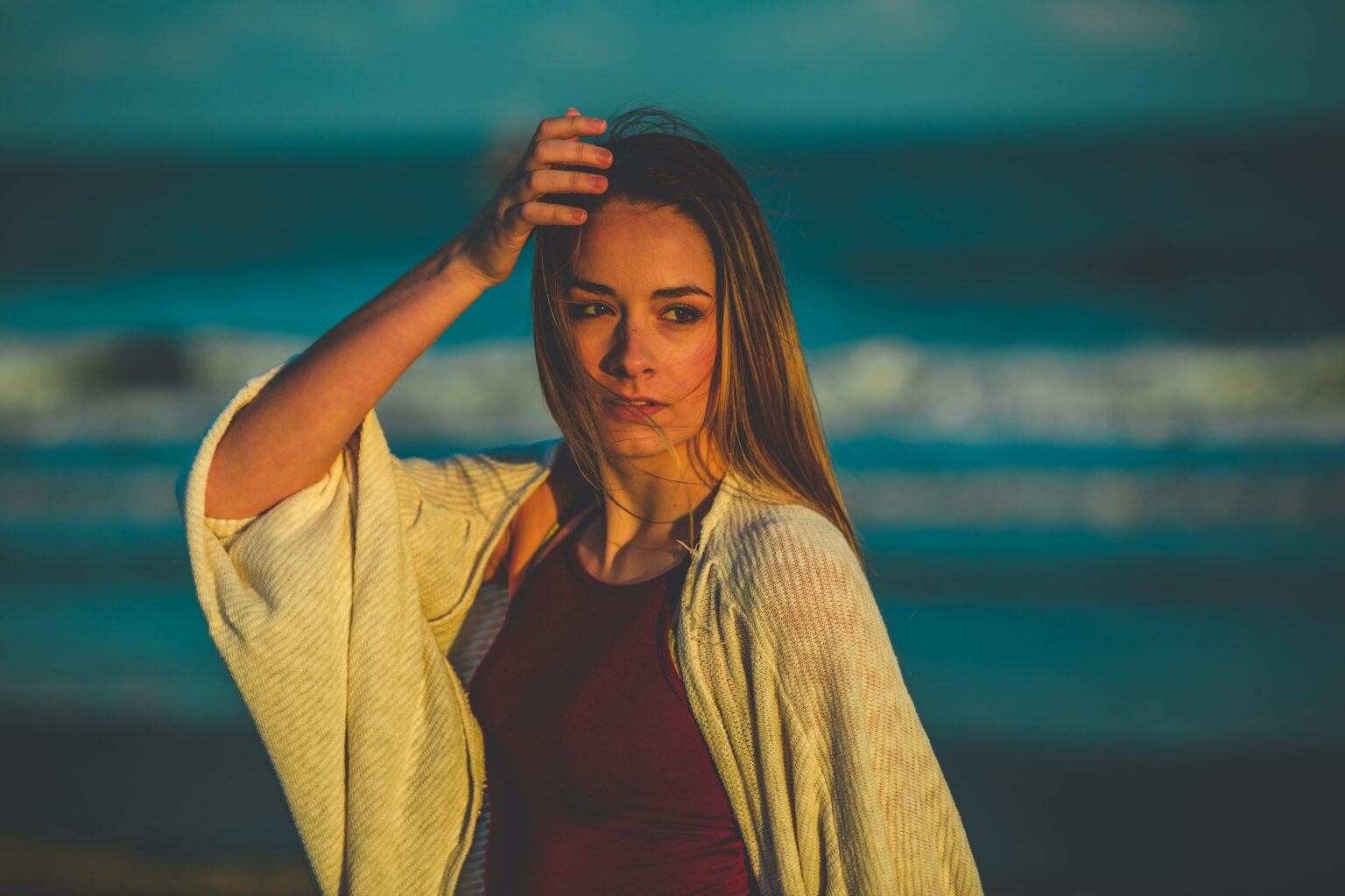 selective focus photography of woman in white cardigan standing near seashore holding her head