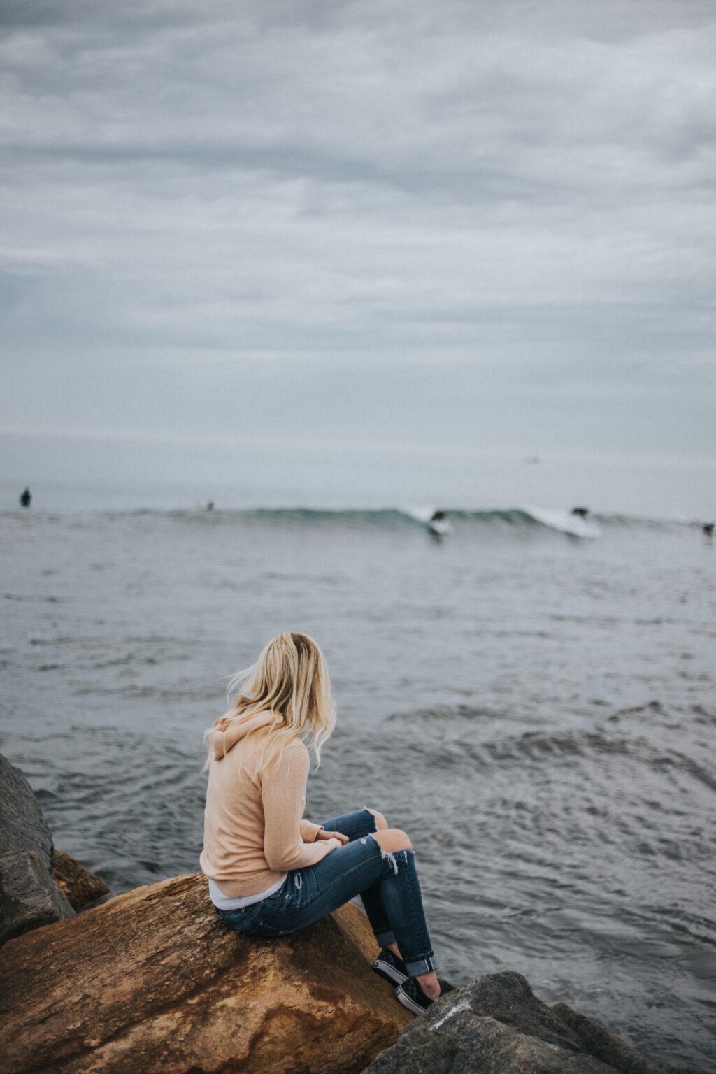 woman sitting on rock near body of water